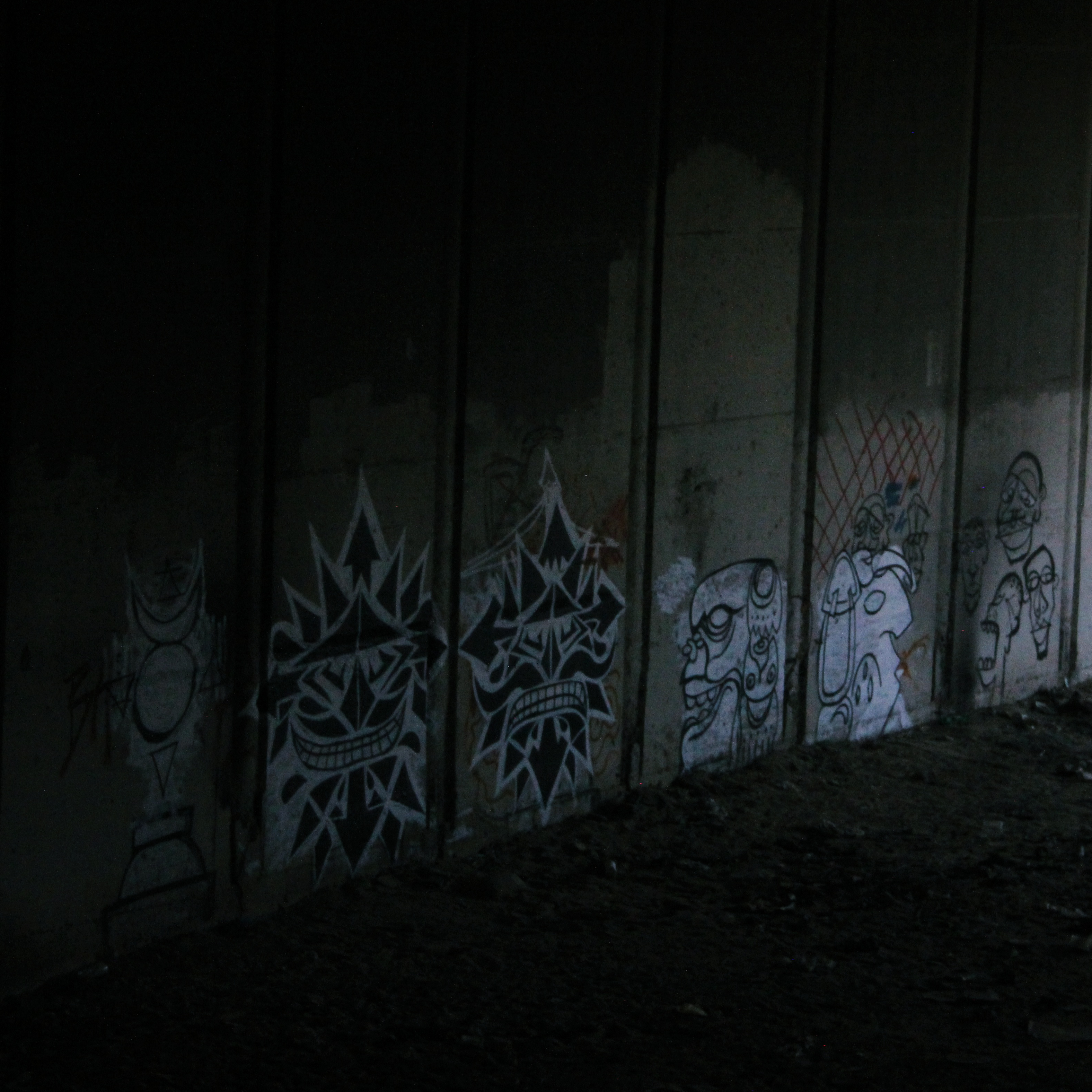 graffiti series of mask-like figures in the shadows under an overpass