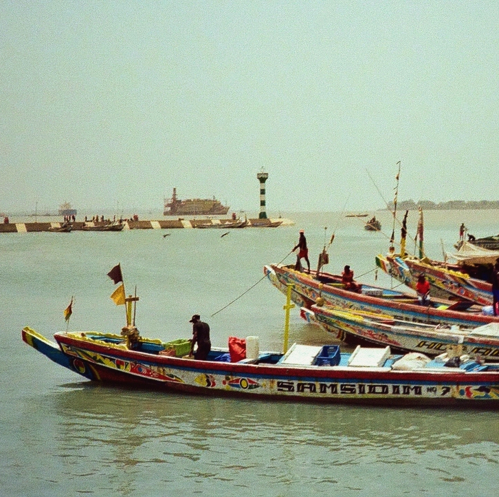 color fishing boats in the green Bissau water with a distant green lighthouse in the background