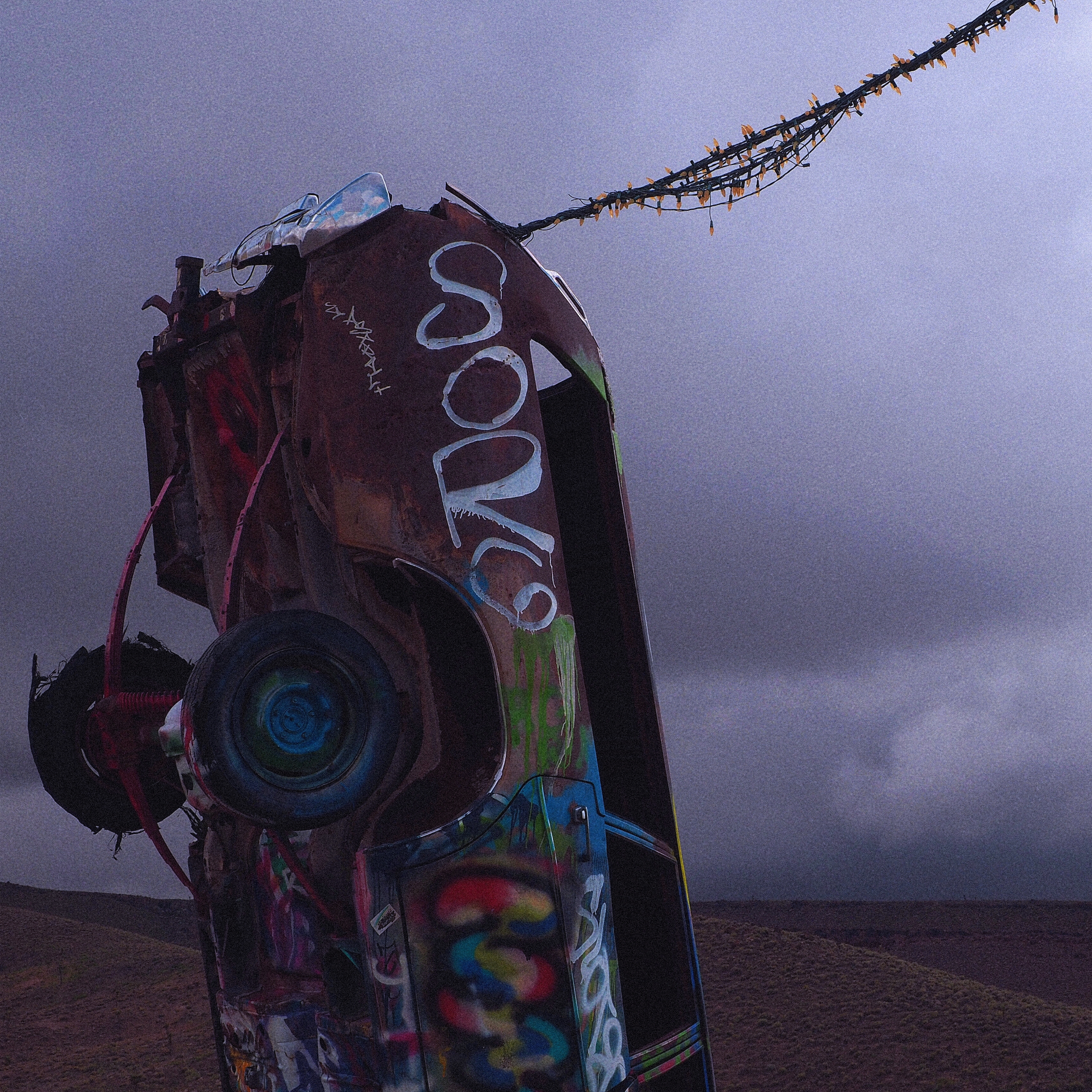 tail end of a ruined, graffiti-riddled car sticking straight up with dense grey clouds in the background