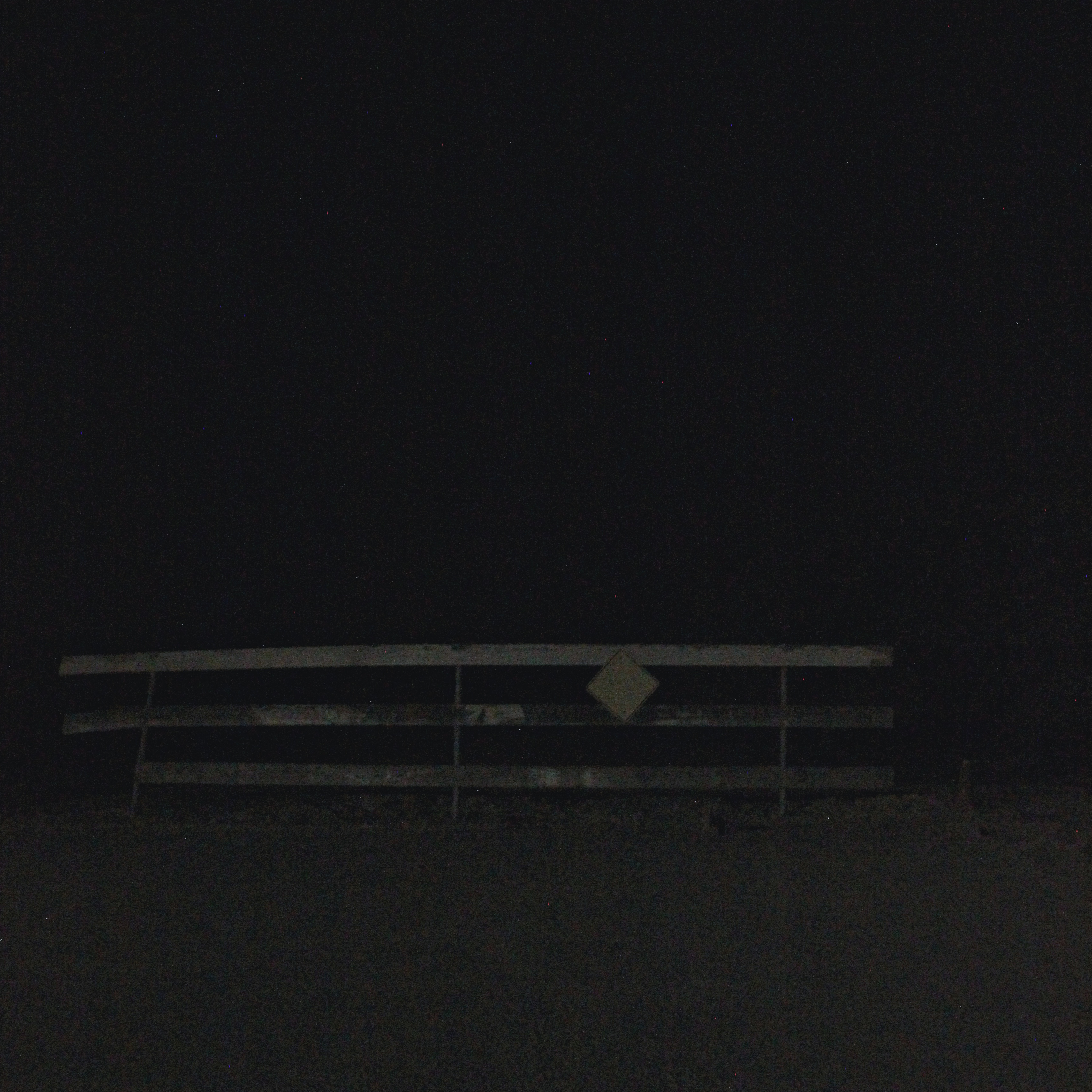 decaying wooden fence with a yellow caution sign attached, barely visible in the pitch-black night