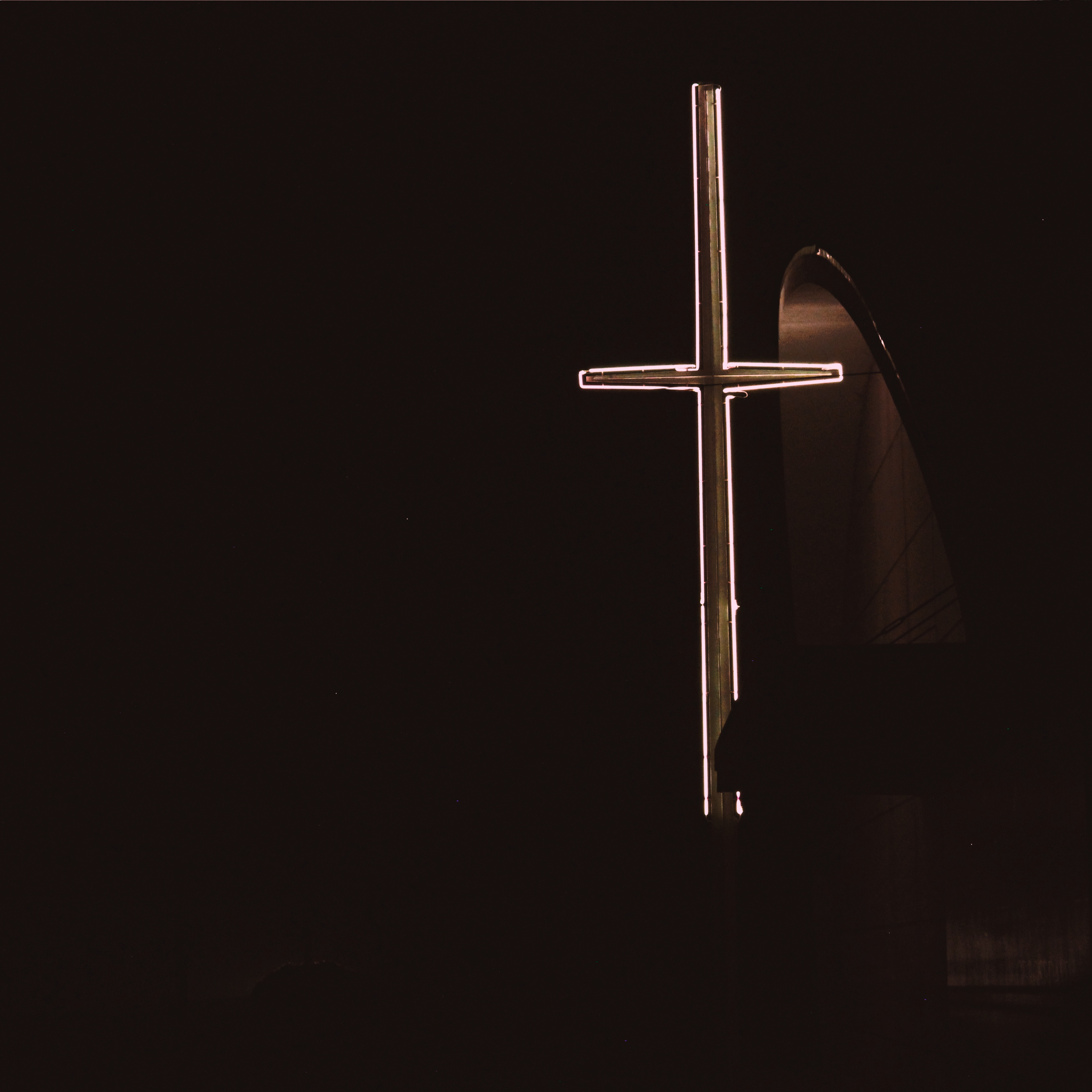 a neon cross attached to a church shining through the pitch black night