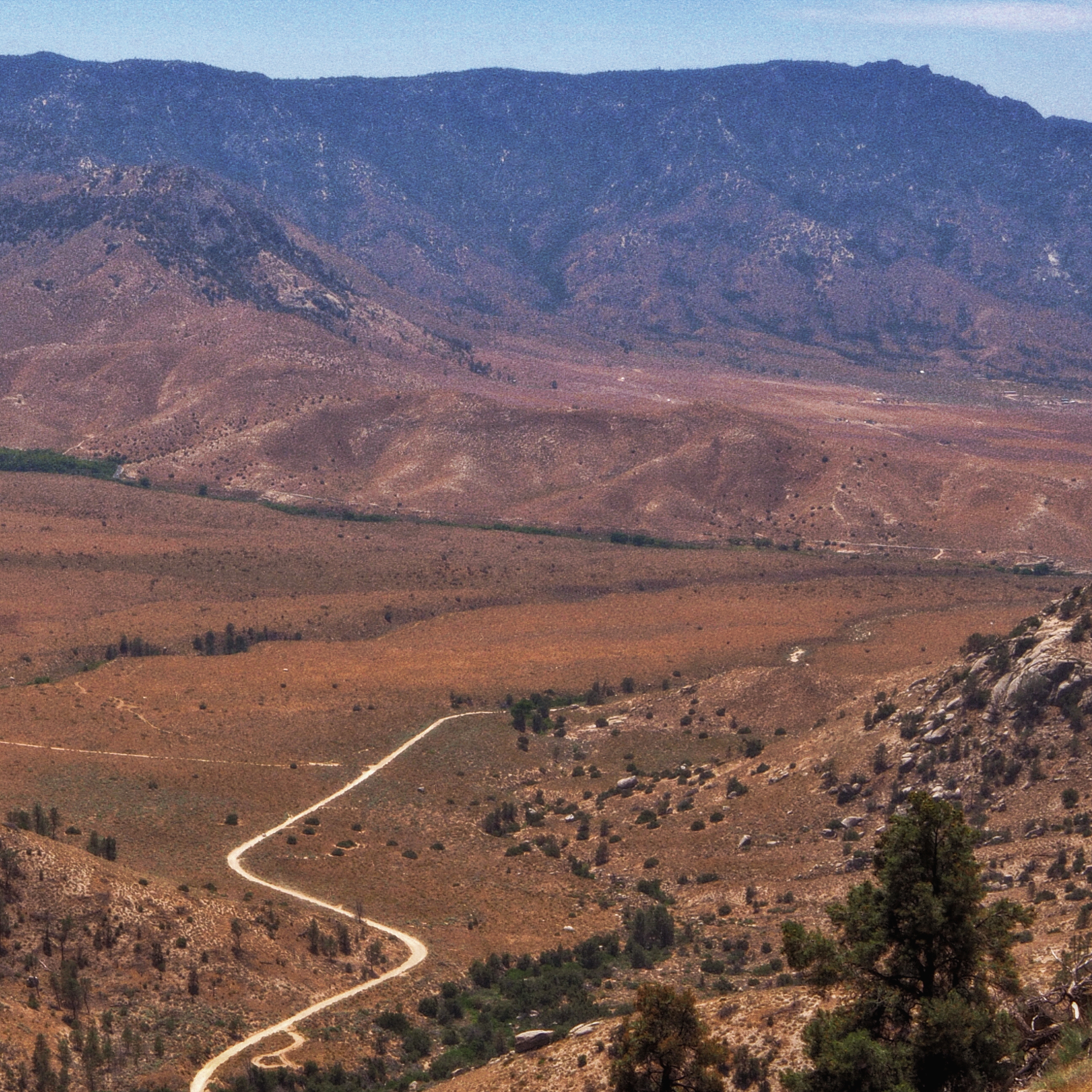 far away view of a desert valley with a winding dirt road snaking through the base