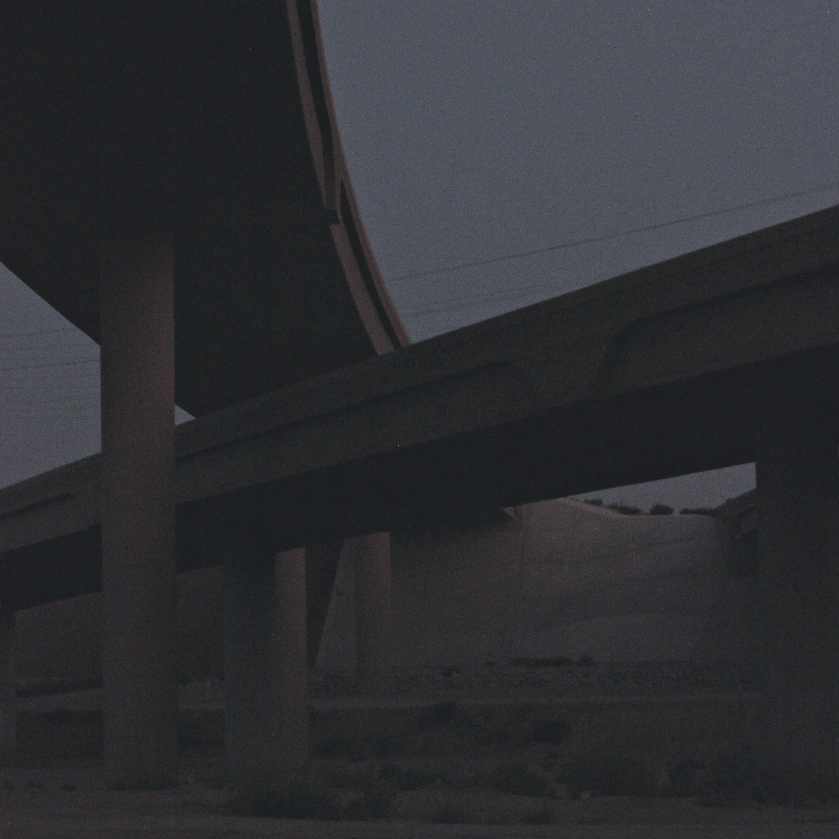two intersecting highway overpasses in the grey twilight with scattered weeds below