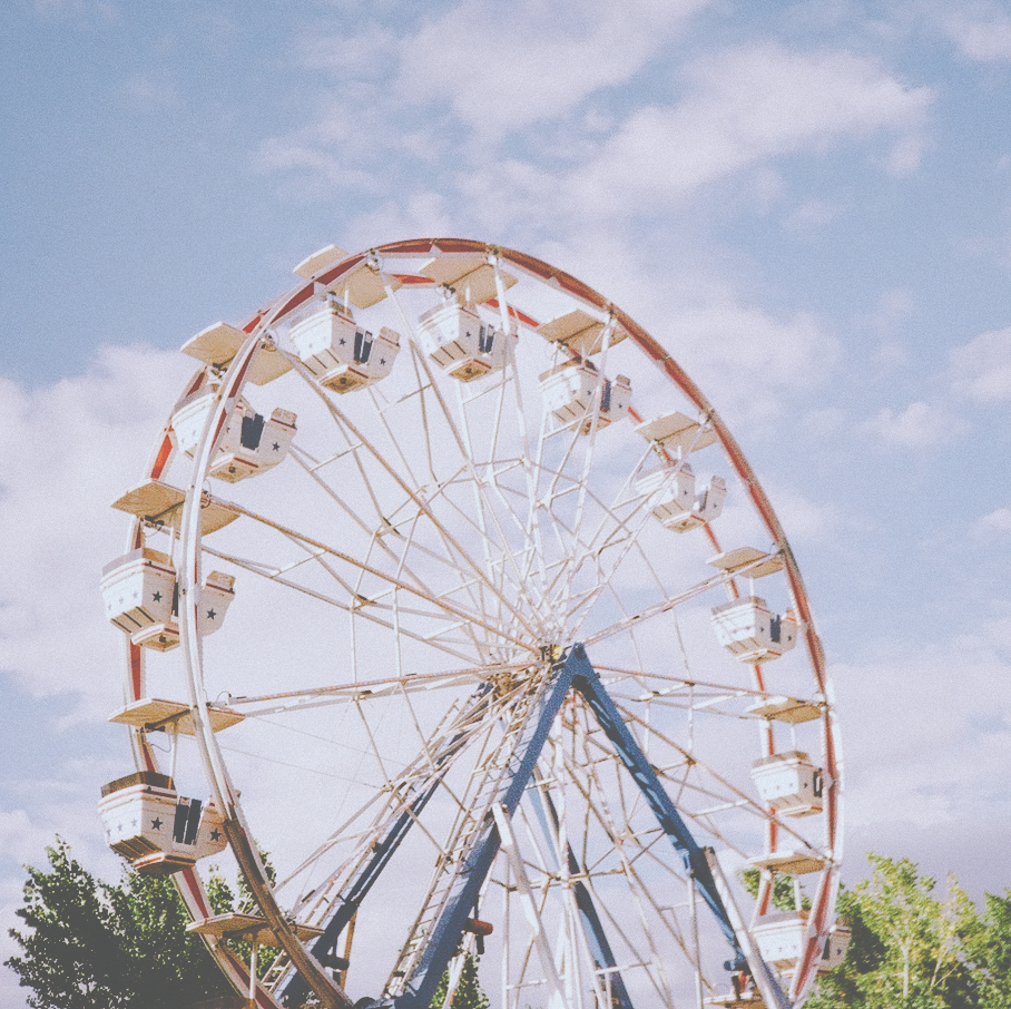 upper third of a ferris wheel with the tops of trees at the bottom and clouds in the background