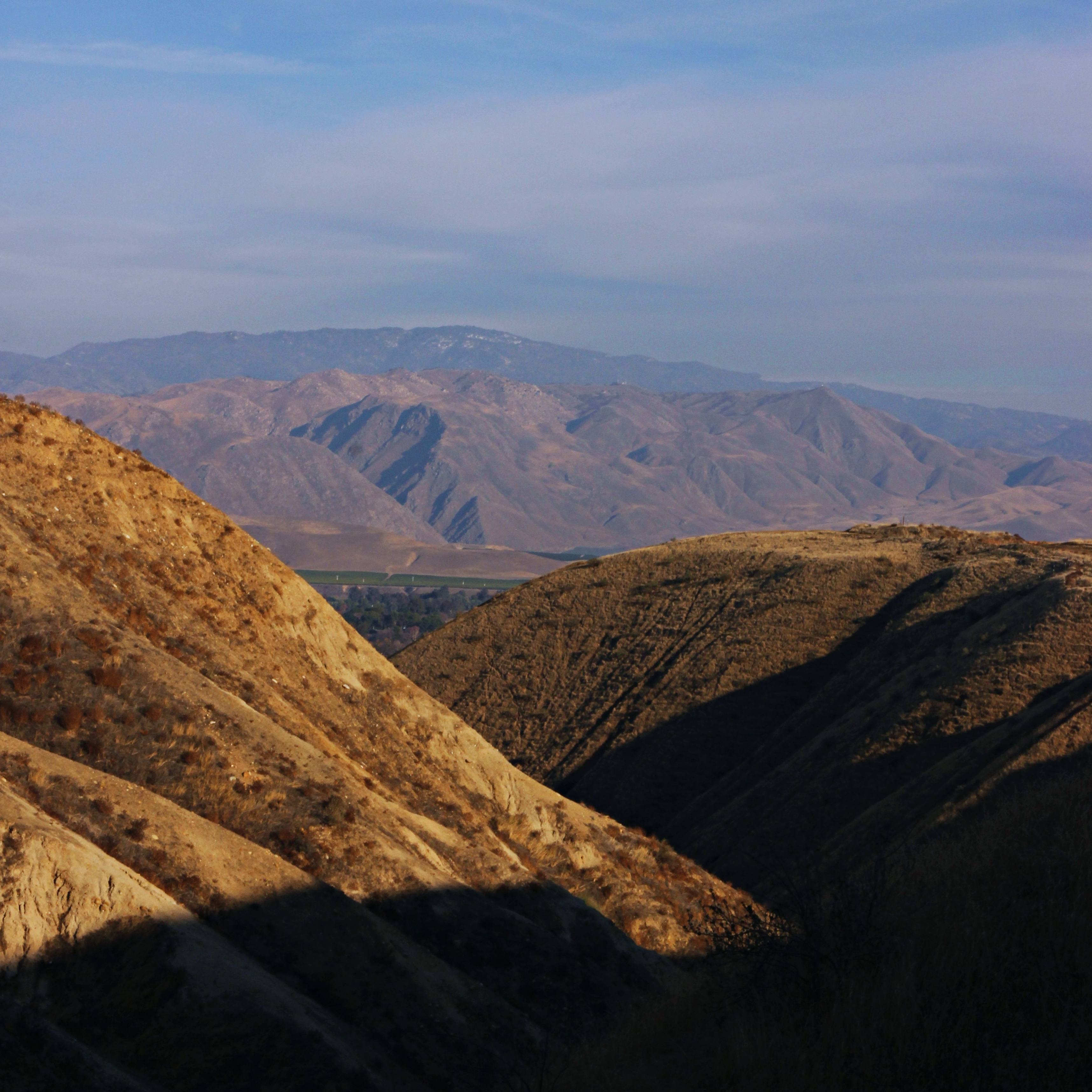 two large hills with the recess between them drenched in shadow and distant mountains in the background