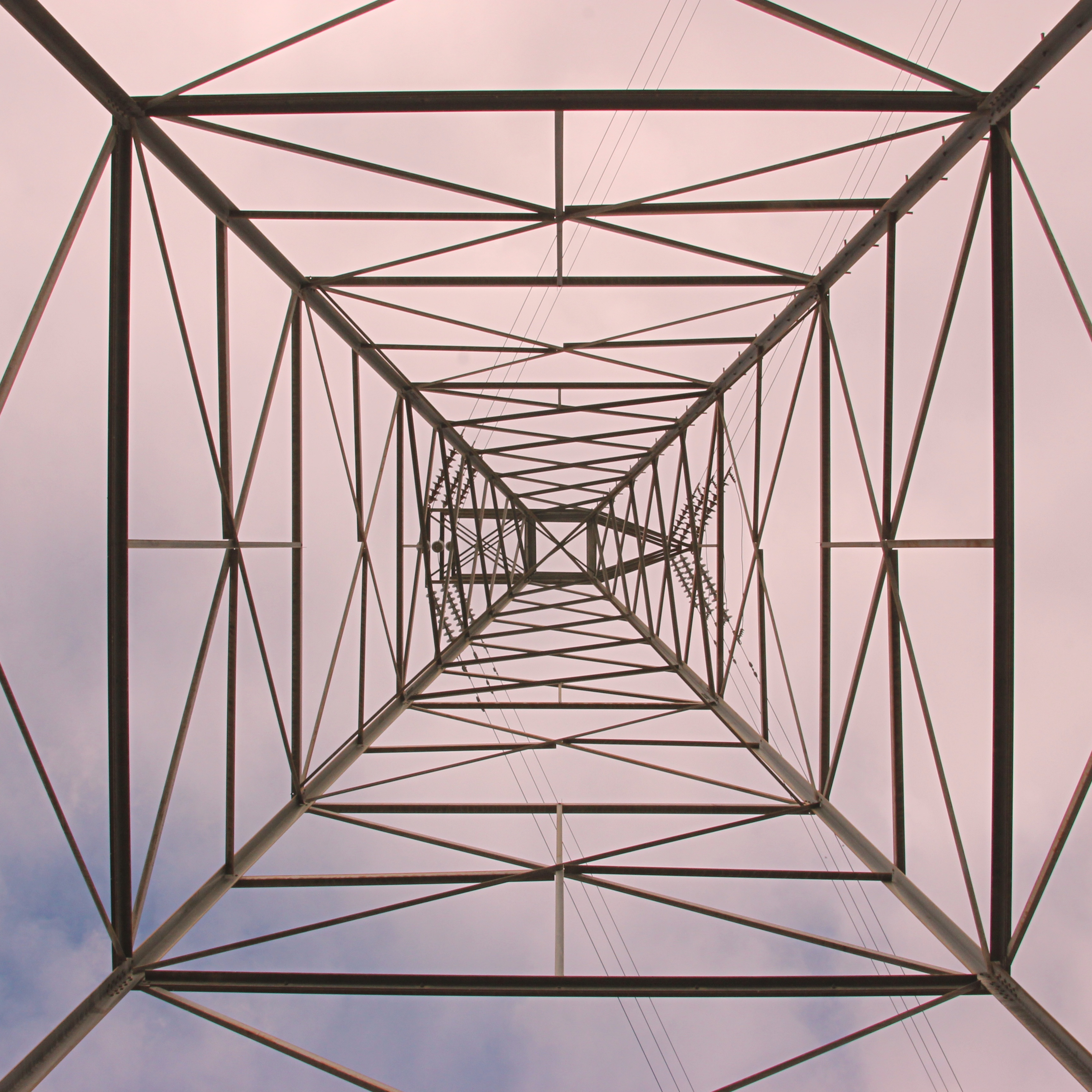 view from directly underneath a large power pylon with an overcast sky above