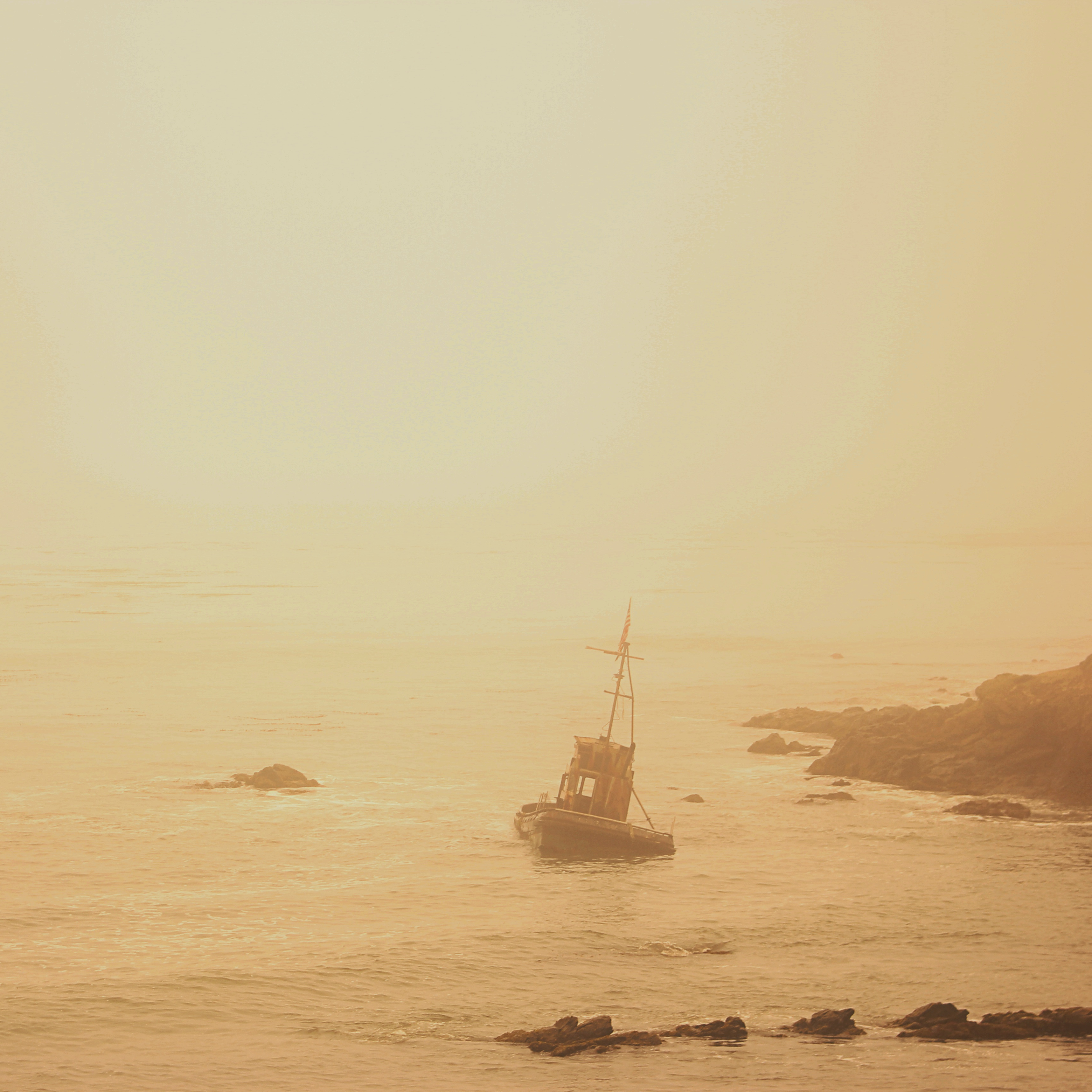 abandoned, half-sunk fishing boat in the ocean surrounded by yellow fog