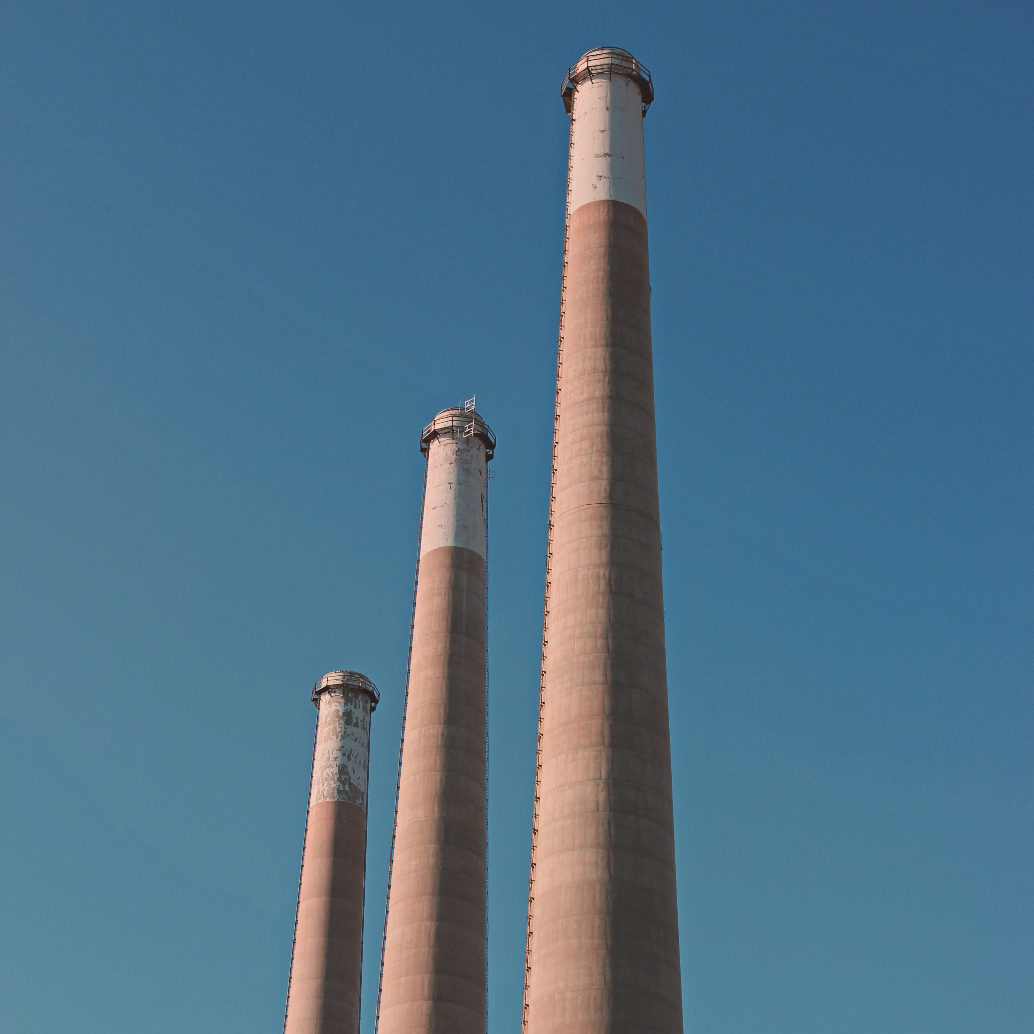 three smokestacks, each just behind the other, framed against a clear blue sky