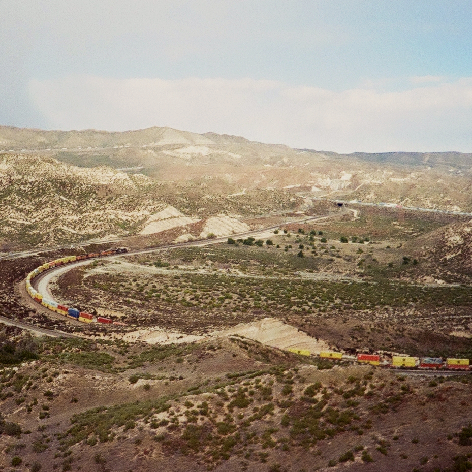 a red and yellow train winding through a sparse desert valley