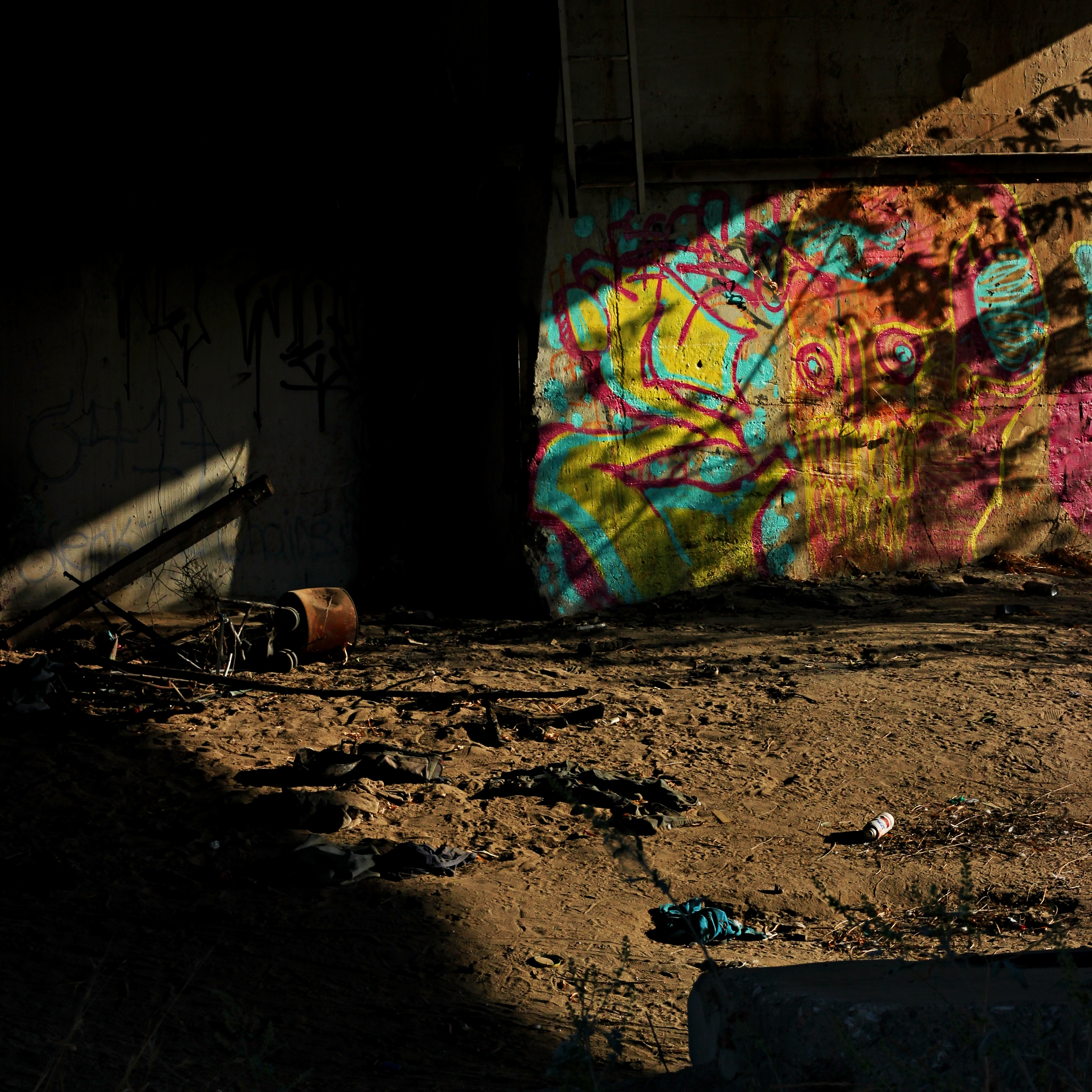 colorful graffiti under an overpass surrounded by shadows and scattered garbage
