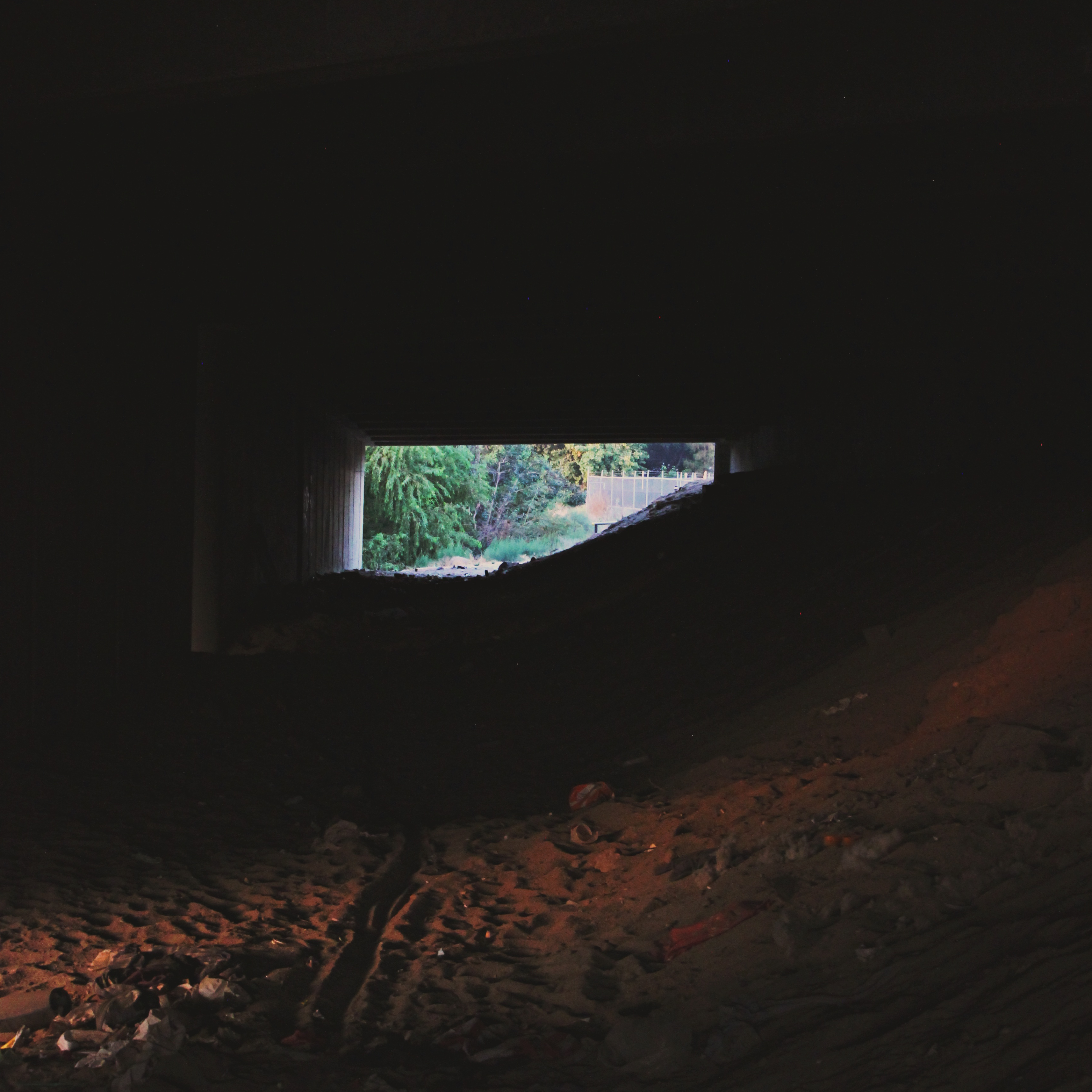 dark, shadowy tunnel underneath an overpass with light and trees just visible on the other side
