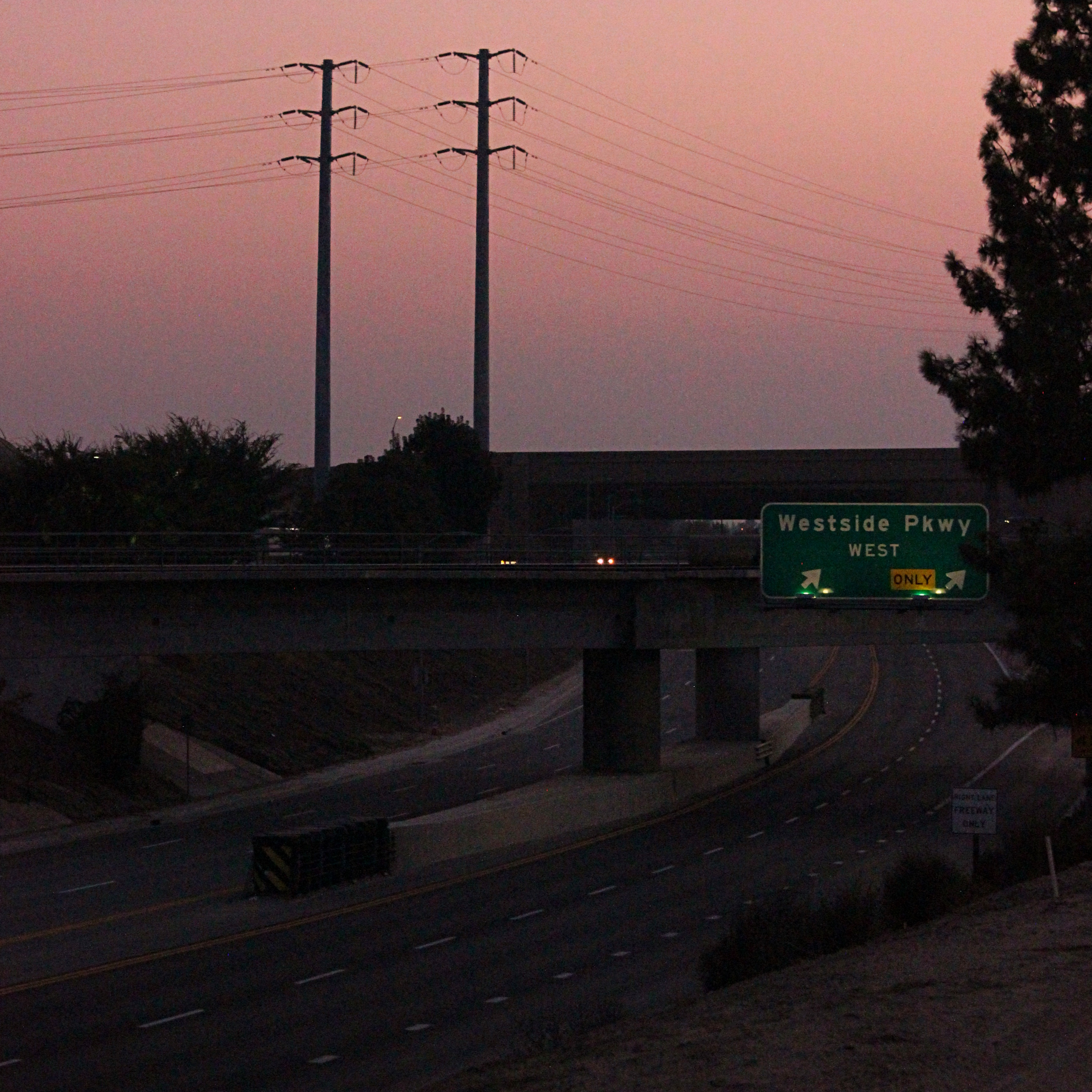 a highway in the pink dawn light with an illuminated street sign two twin power line poles beyond